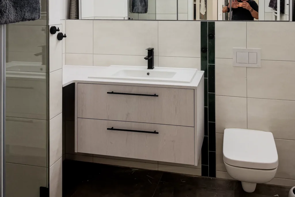 Waschtisch mit eingelassenem Waschbecken und Schubladenmöbel, Spiegel im Bad; daneben WC