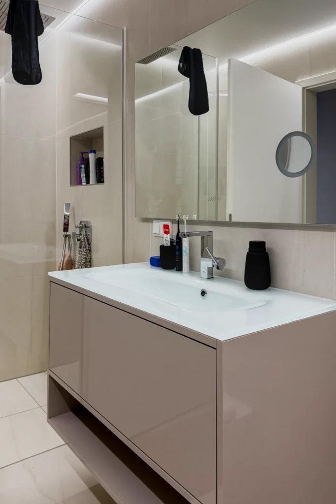 Waschtisch mit eingelassenem Becken, Spiegel und Armatur im modernen Badezimmer; daneben eine Glastürdusche mit Handtüchern.