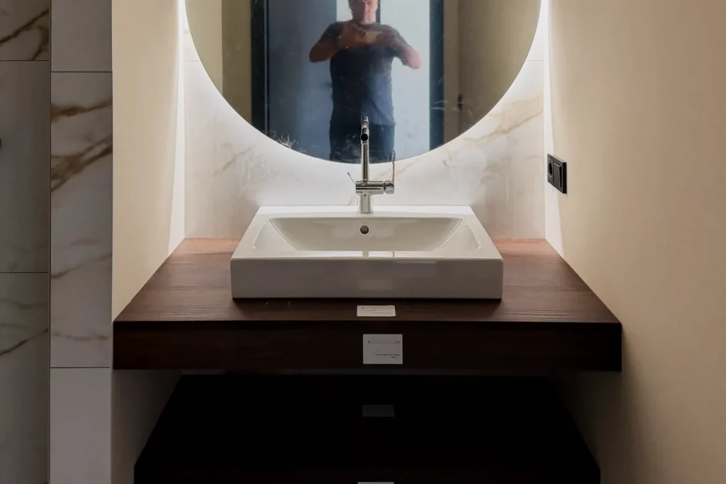 Waschtisch im Badezimmer mit rechteckiger Schüssel, Armatur und Spiegel über der Waschtischplatte