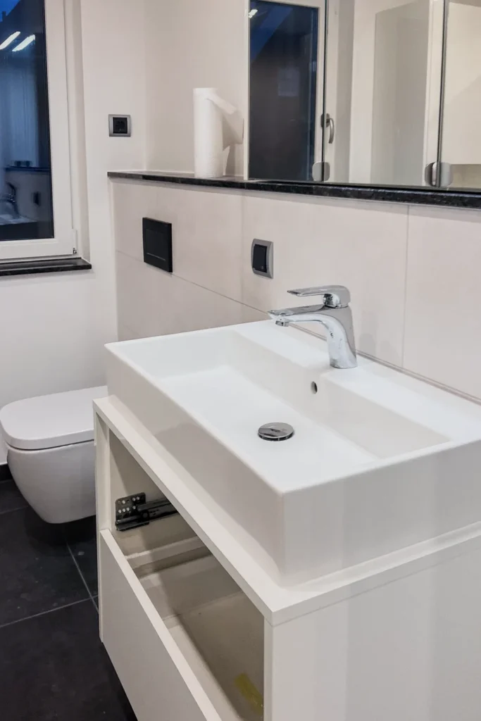 Weiße Küchenarbeitsplatte mit eingelassenem Spülbecken und Armatur, darunter Schublade mit Einsatz.