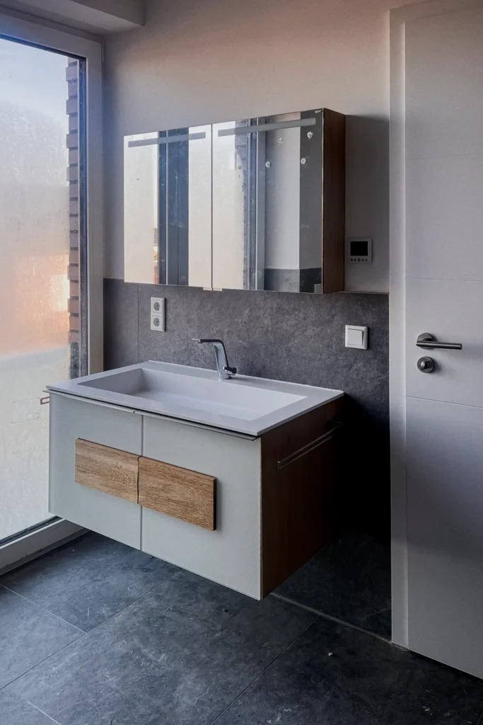 Waschtisch mit Einbaubecken, Unterschrank und Spiegelschrank in grauer Fliesenwand, Fliesenboden.