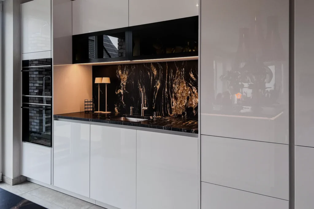 Moderne Einbauküche mit weißer Front, eingelassener Spüle und dunkler Rückwand mit Lichteffekt.