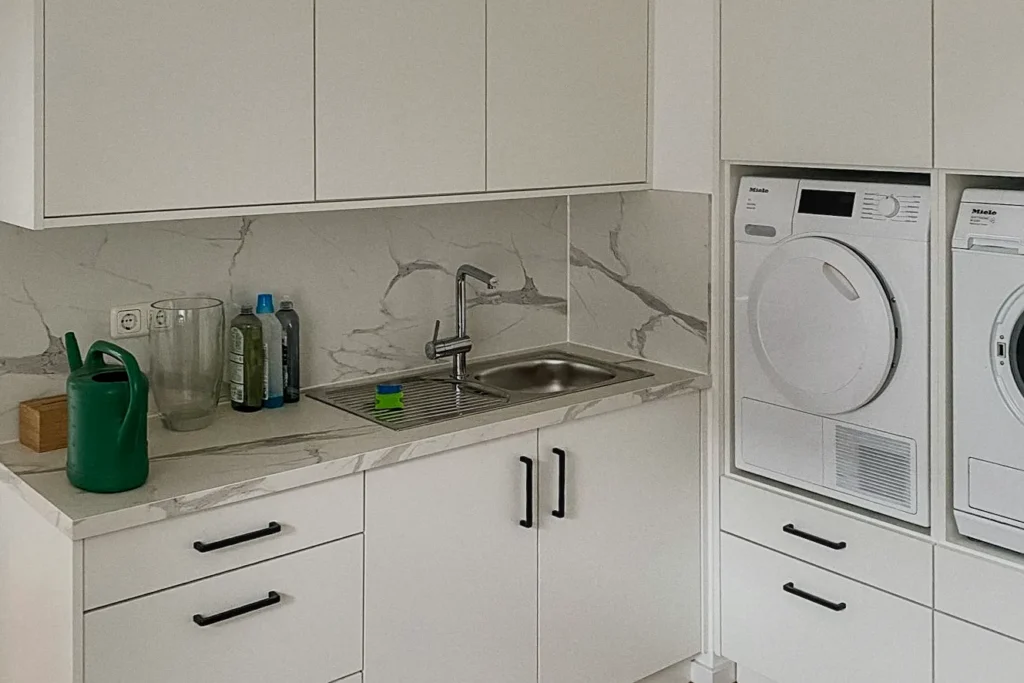 Weiße Küchenzeile mit Spüle, Arbeitsplatte und eingebauten Miele-Waschmaschinen neben Schrankfronten