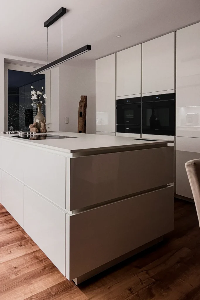 Moderne Kücheninsel mit weißen Schubkästen und dunklen Fronten, ergänzt durch Einbau-Backofen im Hochschrank.