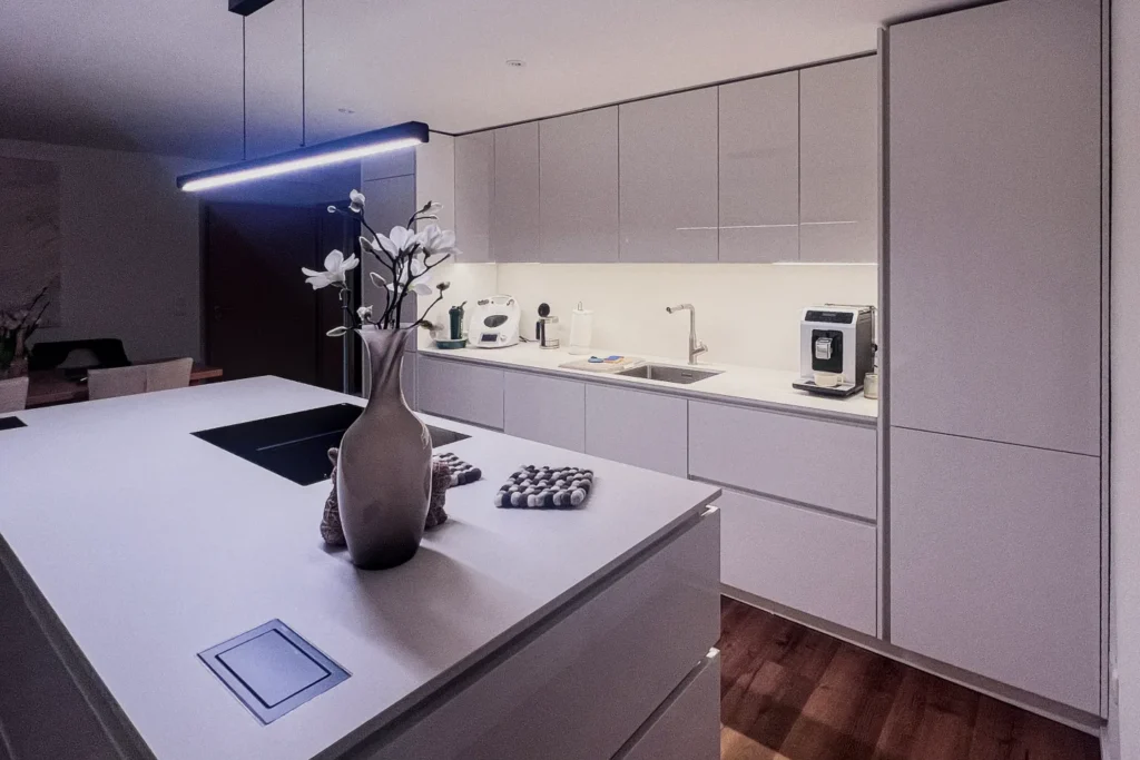 Moderne Küchenzeile mit glatten Schränken, beleuchteter Arbeitsplatte, Spüle und Kaffeemaschine