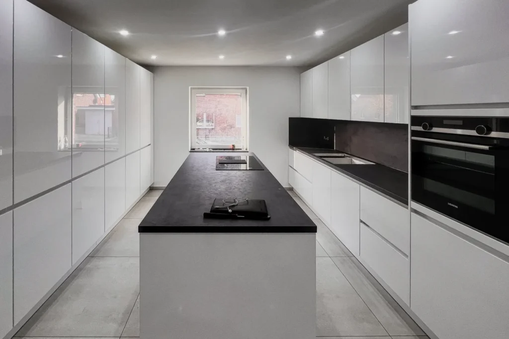 Moderne Küche mit weißen Schränken, dunkler Arbeitsplatte, Kochfeld und eingebautem Backofen.