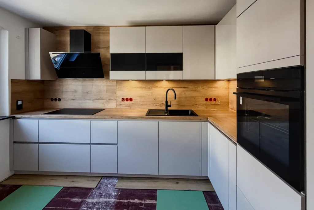 Moderne Einbauküche mit weißen Fronten, Holzrückwand, schwarzem Kochfeld, Dunstabzug und Backofen.
