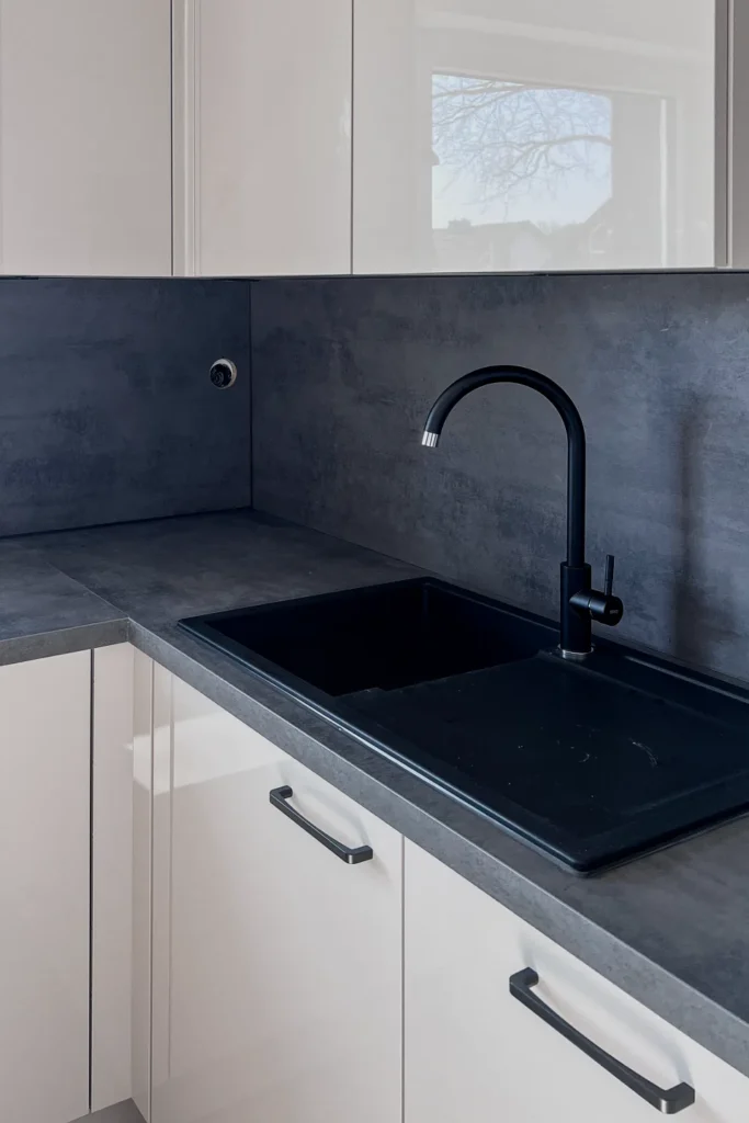 Schwarze Küchenarbeitsplatte mit eingelassenem Spülbecken und Wasserhahn, darunter weiße Schubladen und Fronten.
