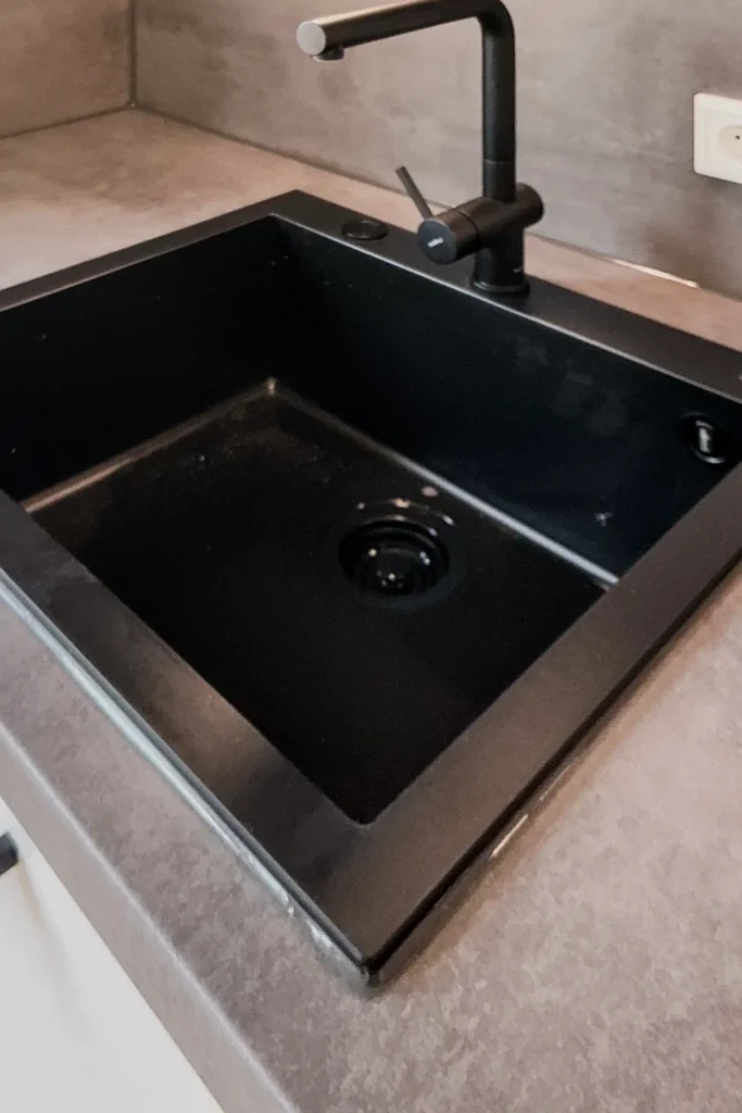 Schwarze Spüle mit Einhebelarmatur und Abfluss, in einer Küchenarbeitsplatte mit schlichten Kanten.