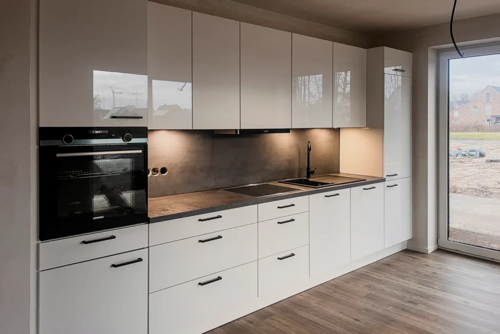 Moderne Küchenzeile mit weißen Fronten, integriertem Backofen, Kochfeld und Edelstahl-Spülbecken.