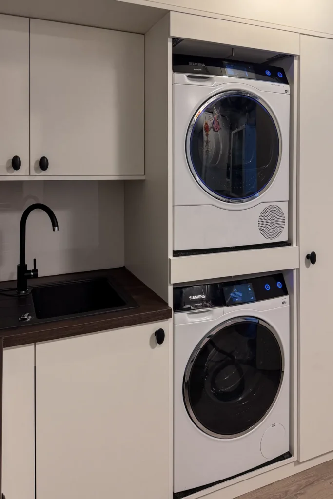 Einbauküche mit Spülbecken, Armatur und Stapel aus Frontlader-Waschmaschine und Trockner mit „Siemens“.
