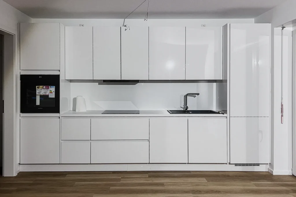 Weiße Einbauküche mit Hochschrank, Backofen, Spüle und Herdzeile, Hängeschränken und Arbeitsplatte.