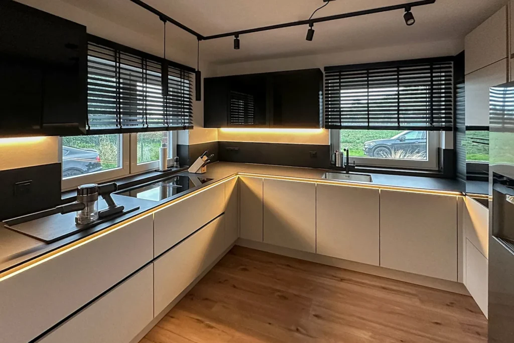 Moderne L-förmige Küchenzeile mit dunklen Hängeschränken, LED-Lichtleisten und Fensterfront