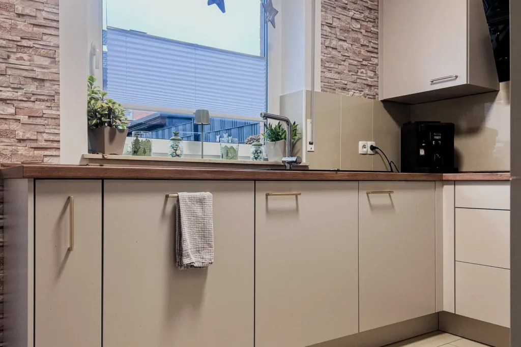 Küchenzeile mit Frontschränken, Spüle unter dem Fenster, Handtuch und Arbeitsplatte mit Pflanzen und Accessoires