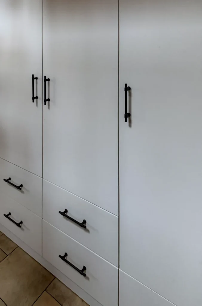 Weißer Küchenschrank mit Schubladen und zwei Türen, schwarze Griffleisten und Türgriffe sichtbar.