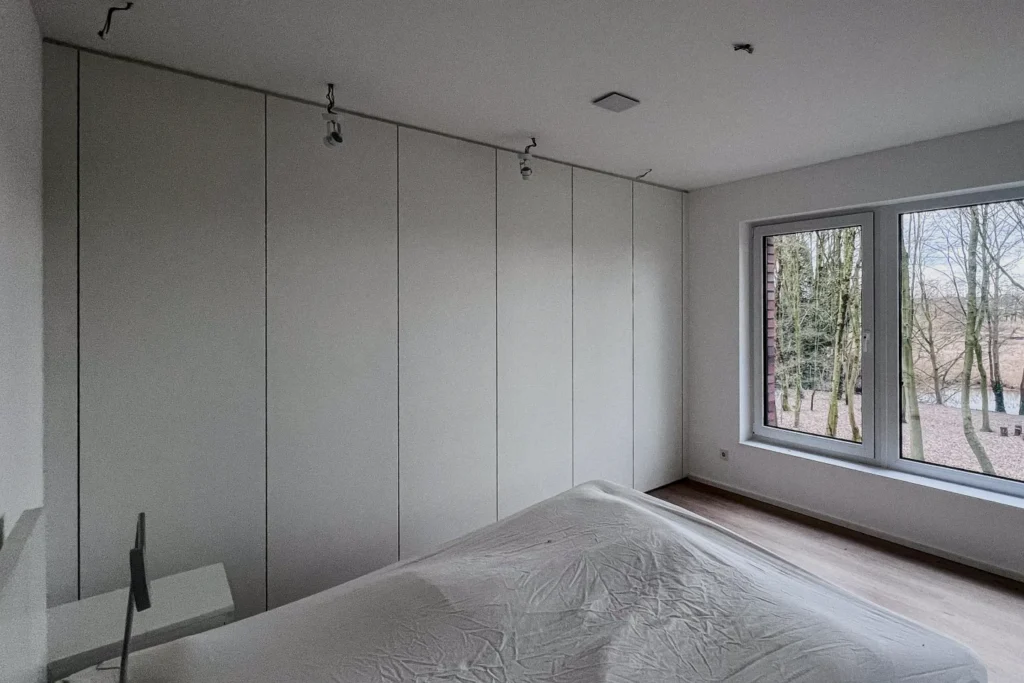 Schlafzimmer mit Einbauschrank, Bett und großen Fenstern an der Wand mit Deckenlampen