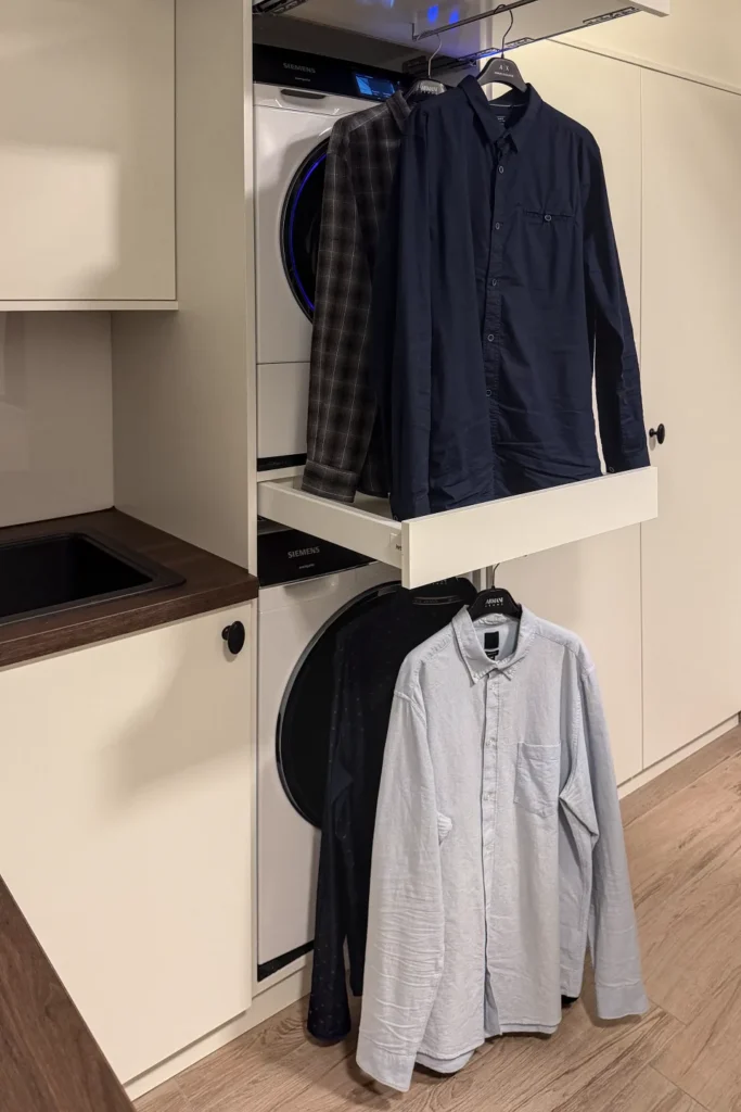 Wäscheschrank mit offener Waschmaschine, daran hängende Hemden und Jacken in der Küche, „Siemens“.