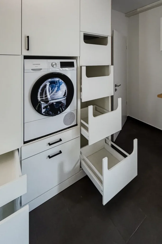 Eingebaute Waschmaschine mit Front in der Küchenzeile, Bedienfeld „SIEMENS“, daneben Auszüge mit Fächern.