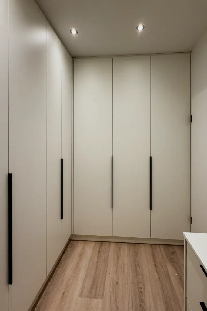 Schrankwand mit flächenbündigen Türen und Griffleisten, Holzlaminatboden und Deckenstrahlern in der Ecke der Küche