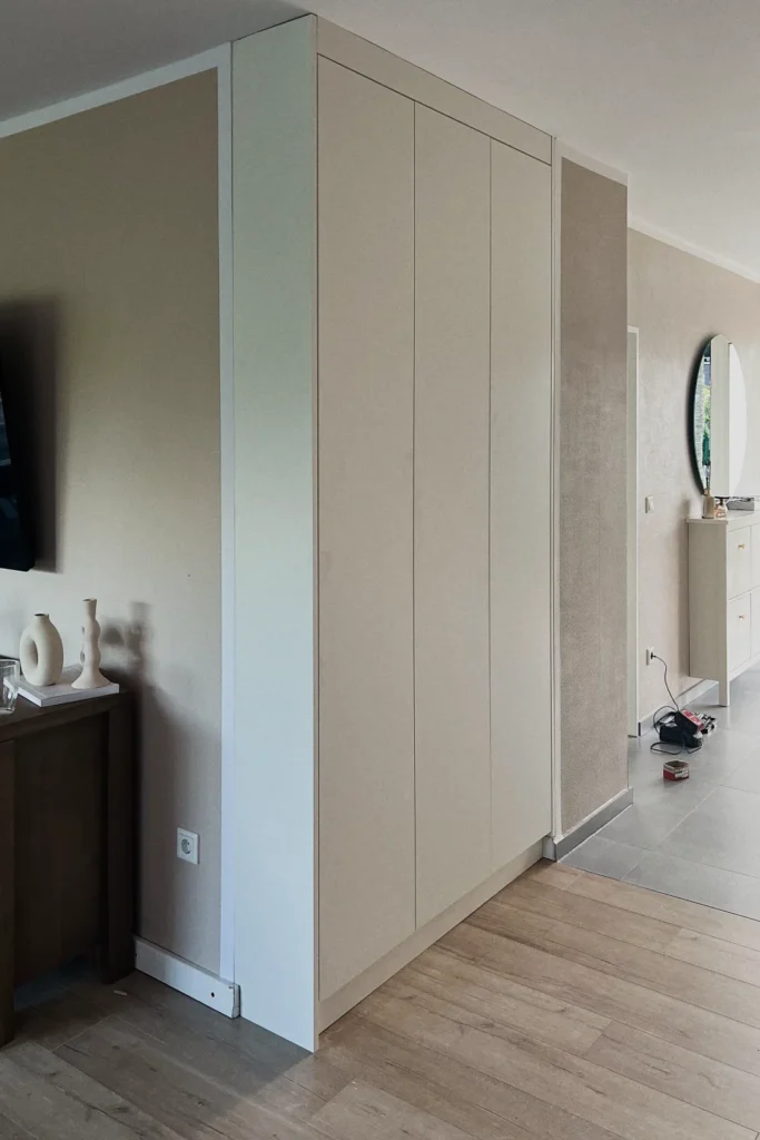Großer Einbauschrank mit glatten Fronten und vertikalen Türpaneelen im Flur, daneben Spiegel und Sideboard
