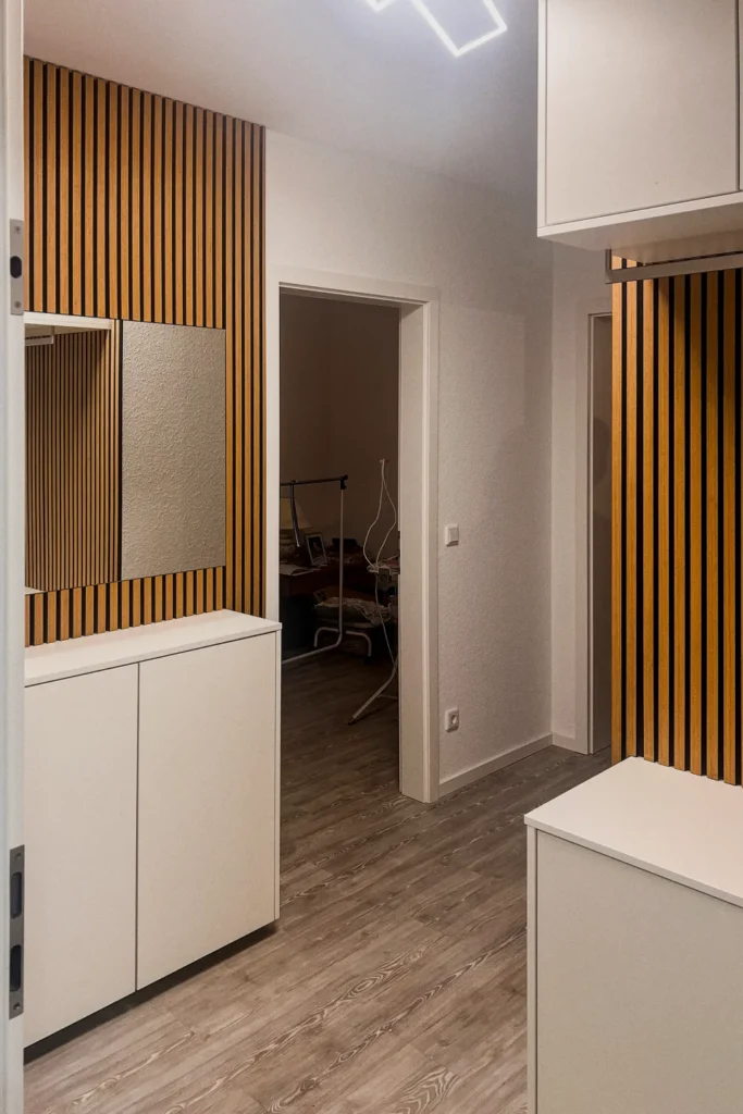 Einbauschrank im Flur mit vertikalen Holzlamellen, weißen Unterschränken und heller Arbeitsplatte