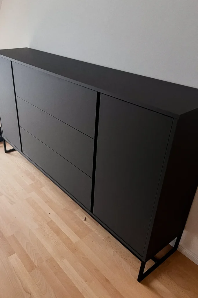 Schwarzes Sideboard mit zwei Türen und mehreren Schubladen im Flur neben dem Holzfußboden.