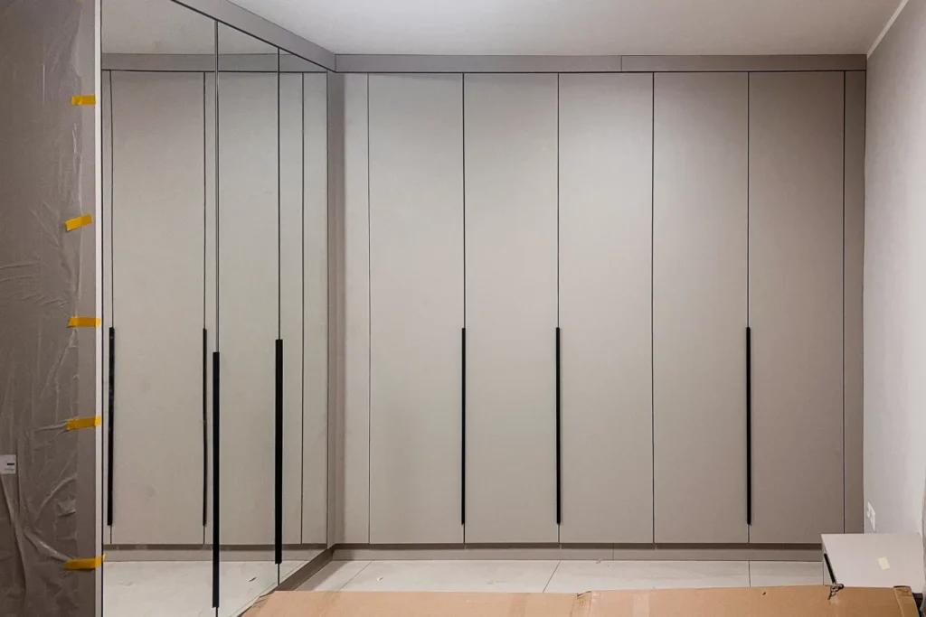 Schrankwand mit vertikalen Fächern und schmalen Griffleisten, weißer Küchenbereich im Innenausbau.