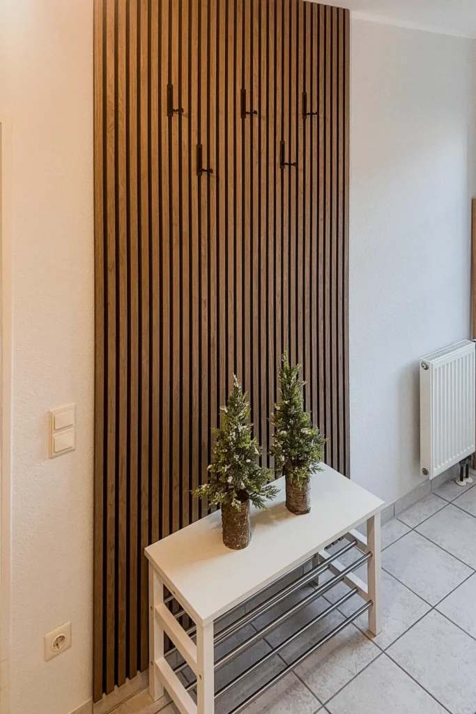 Holz-Lamellentür neben weißer Bank mit Metallablage und zwei kleinen Pflanzenvasen.