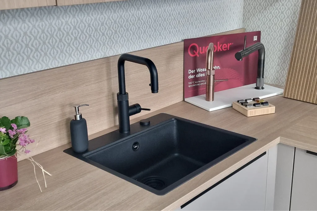 Schwarzes Küchenspülbecken mit Armatur auf hellem Küchenarbeitsplatte, Werbeaufsteller mit „Quooker“.