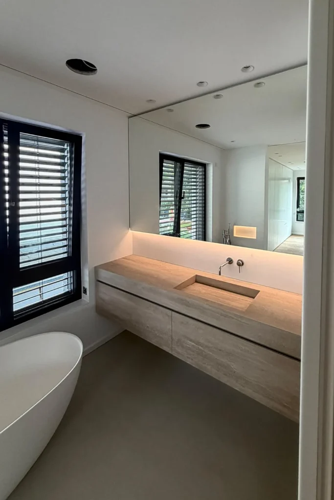 Moderne Badezimmer-Waschtischplatte mit eingelassenem Spülbecken, Schrankfronten und Spiegel, Fenster mit Rollläden.