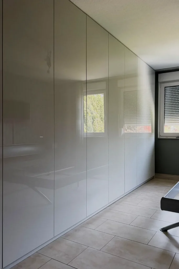 Heller Hochschrank mit geschlossenen Fronten in einer Nische unter schräger Decke neben Fenstern