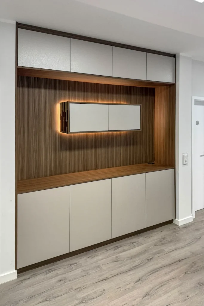 Einbauschrank mit Holzfronten, weißen Türen und beleuchteter Nische mit Spiegel in der Küche.
