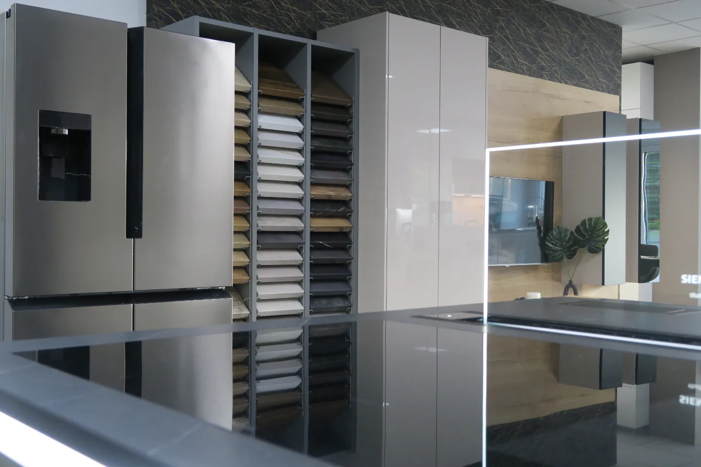 Moderne Küche mit hochgebautem Schrank, geöffnetem Auszugregal, weißen Fronten, dunkler Marmor-Rückwand, Arbeitsplatte und Aufdruck „SIEMENS“.